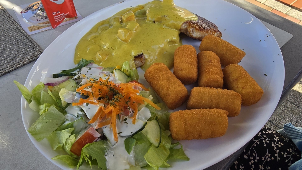 Ein Teller mit Curry-Sauce, einem frischen gemischten Salat und mehreren frittierten Croquettes.