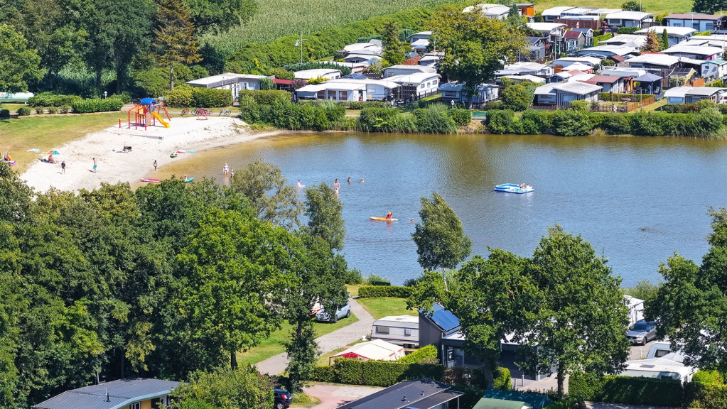 Ein ruhiger See, umgeben von dichtem Wald und Wohnhäusern an einem sonnigen Tag.